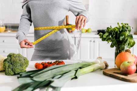 cropped view of woman measuring waist near vegetables on table