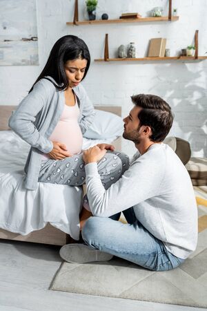 handsome man hugging pregnant african american woman in pajamasの写真素材