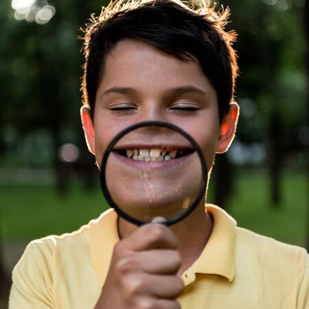 selective focus of cheerful boy holding magnifier near face