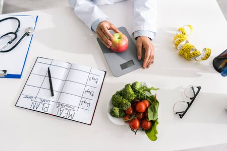 top view of nutritionist holding apple on food scales near vegetablesの写真素材