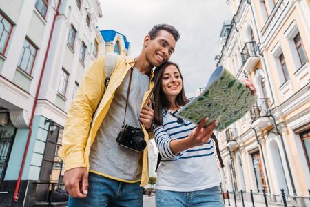 low angle view of happy mixed race man looking at map near happy girl