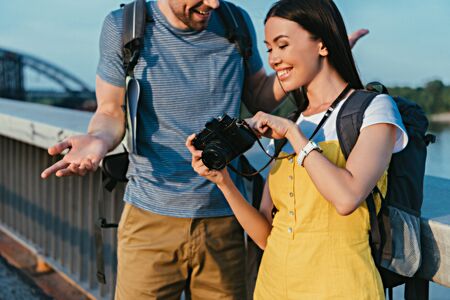 cropped view of man and asian woman in overalls looking at digital cameraの写真素材