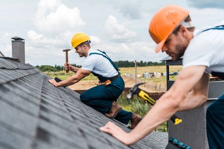 selective focus of handsome handyman repairing roof with colleague