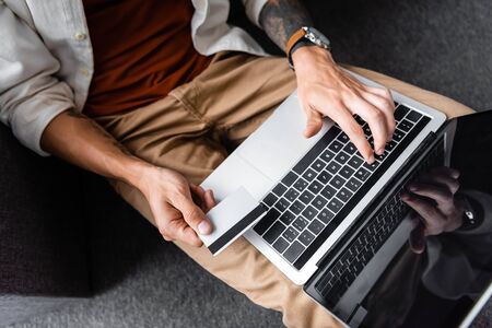 cropped view of man holding credit card and using laptop in apartmentの写真素材