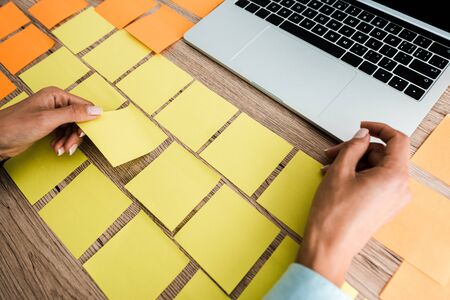 cropped view of woman touching sticky note near laptop on desk