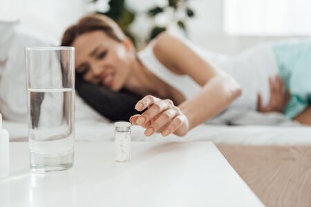 selective focus of suffering woman in bed and pills with glass of water on foregroundの写真素材