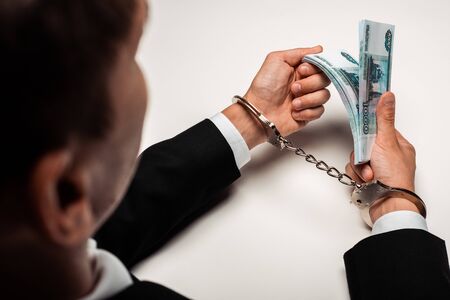 selective focus of businessman in handcuffs holding bribe on whiteの写真素材