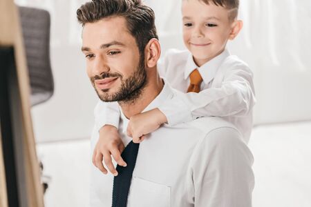 cheerful boy embracing bearded dad in white shirt at homeの写真素材