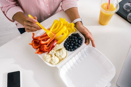 top view of woman holding plastic fork near vegetables in food container