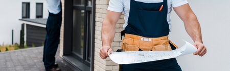 panoramic shot of architect holding blueprint near coworker