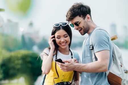 handsome man and asian woman smiling and looking at smartphone