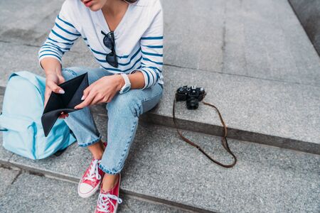 cropped view of young woman holding empty wallet near digital camera on stairs