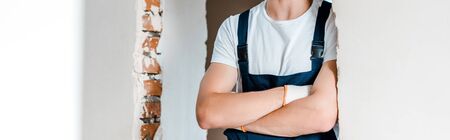 panoramic shot of repairman standing with crossed arms in house