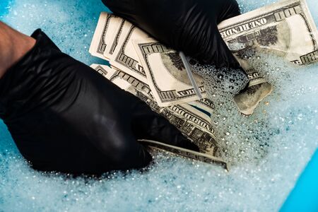 cropped view of man in black rubber gloves washing dollar banknotes in soap bubbles with waterの写真素材