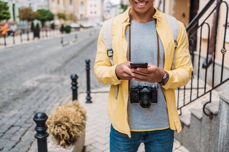 cropped view of happy mixed race man using smartphone outside
