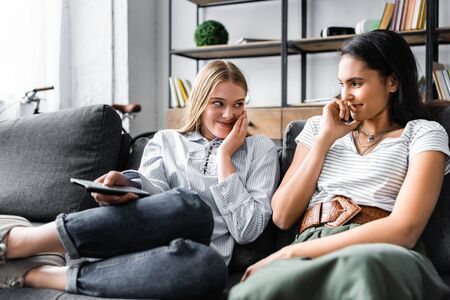 multicultural friends holding remote controller and smiling in apartment