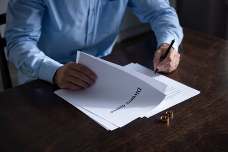 partial view of man sitting at table and signing divorce documents