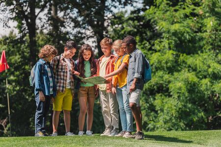 happy group of multicultural kids looking at map near trees in parkの写真素材