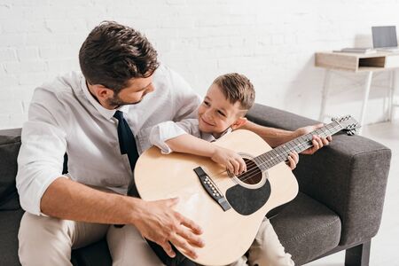 dad teaching son to play acoustic guitar at homeの写真素材