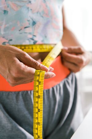 selective focus of of sportive woman measuring waist