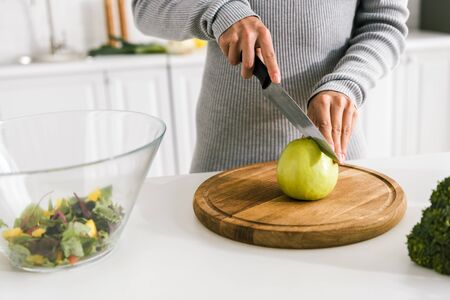 cropped view of girl holding knife near green whole appleの写真素材