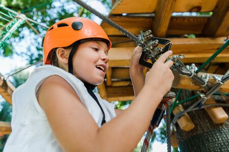 low angle view of happy kid in helmet touching safety equipment in adventure park