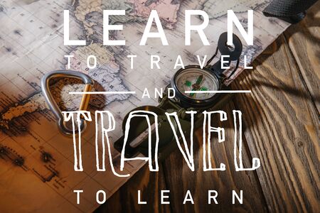 compass, safety hook and map on wooden table with learn to travel and travel to learn illustration