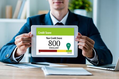 selective focus of happy man holding digital tablet with your credit score lettering in office