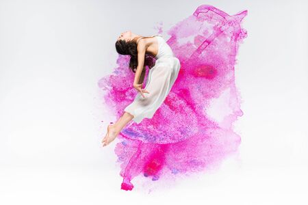 beautiful ballerina in white dress dancing in purple and pink paint splashes and spills on grey backgroundの写真素材