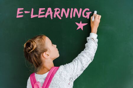 schoolchild holding chalk near chalkboard with e-learning lettering on green