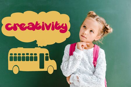 pensive kid standing with backpack near chalkboard with school bus and creativity lettering on greenの写真素材