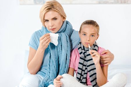 sick mother holding tissue near ill kid with digital thermometerの写真素材