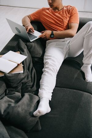 cropped view of young man lying on sofa and using laptop at homeの写真素材