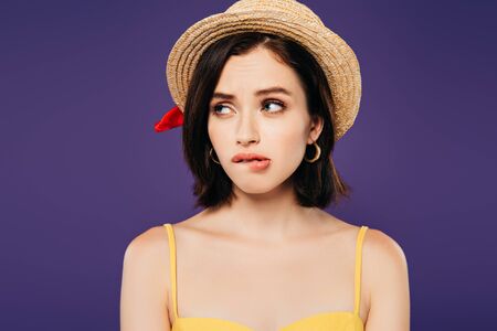 confused girl in straw hat looking away isolated on purpleの写真素材