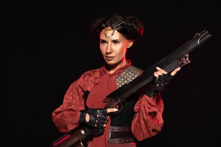 confident steampunk girl in leather gloves holding gun isolated on black