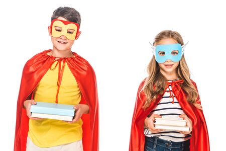 front view of two smiling kids in masks and hero cloaks holding books isolated on whiteの写真素材
