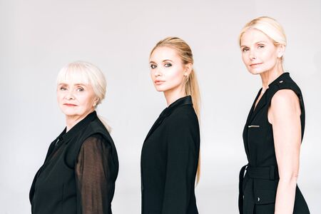 side view of three-generation blonde women in total black outfits isolated on grey