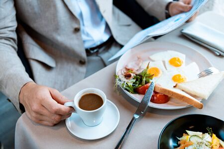 cropped view of businessman holding cup of coffee and reading newspaper in cafeの写真素材