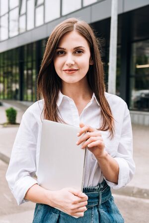 attractive young woman in white shirt holding laptop on streetの写真素材
