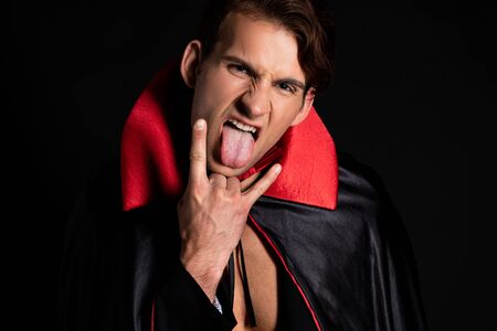 man in vampire halloween costume sticking out tongue and showing rock sign isolated on blackの写真素材