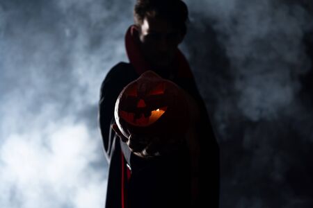 selective focus of man holding pumpkin on black with smoke