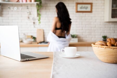 selective focus of laptop, cup of coffee and basket with buns on table with girl on backgroundの写真素材