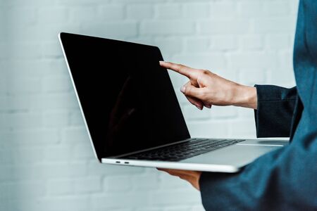 cropped view of woman pointing with finger at laptop with blank screen 