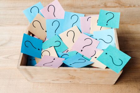 overhead view of sticky notes with question marks in wooden box on deskの写真素材