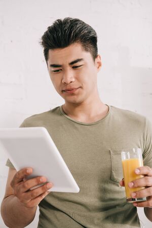 handsome asian man reading fake news newspaper while holding glass of orange juiceの写真素材