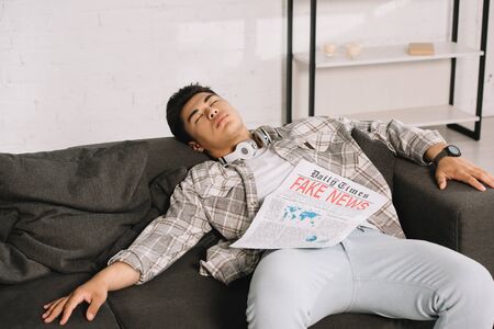 tired asian man sleeping on sofa at home with fake news newspaperの写真素材
