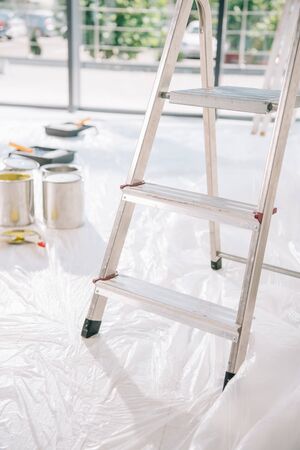 selective focus of ladder in room with cans of paint on white floor covered with cellophaneの写真素材