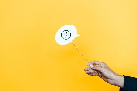 cropped view of woman holding stick with speech bubble with sad face on orange