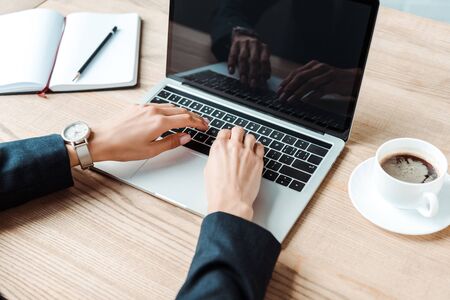 cropped view of businesswoman typing on laptop near cup with coffee on table の写真素材