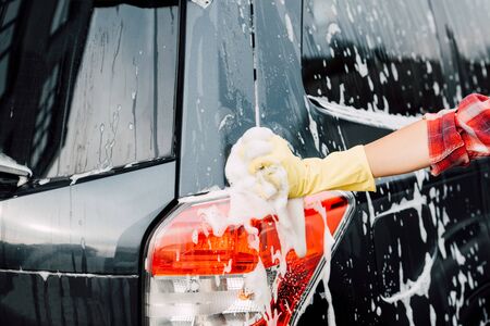 cropped view of girl in latex glove near wet car in foamの写真素材